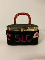 Front view of needlepoint box purse featuring 'SLC' floral design and Bakelite handle.