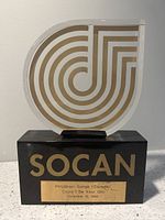Full front view of the SOCAN award showing lucite plaque with gold and white concentric design on a black base with brass nameplate.