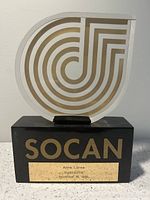 Front view of SOCAN music award showing lucite top with gold pattern and black base with 'SOCAN' in gold lettering plus brass name plate with engraving.