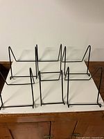 Six black metal wire square display stands arranged on a white surface, showing their size and shape.