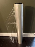 Full view of the tall industrial roll of clear cello wrap standing upright with some wrap unraveled on the side.