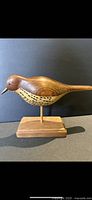 Side view of a finely carved wooden wood thrush bird on a rectangular base against a dark background.