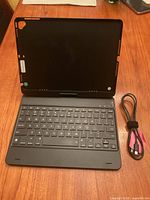 Black keyboard case open with visible keyboard layout, charge cable coiled neatly beside it