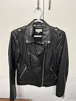 Front view of black faux leather jacket showing front zipper, zippered pockets, buttoned epaulets and collar details.