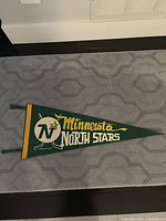 Full view of green felt pennant with Minnesota North Stars logo and lettering laid flat on grey surface.