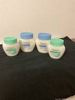 Four jars of Ponds skincare products on black cloth; two with blue lids (Dry Skin Cream) and two with green lids (Cold Cream Makeup Remover) shown clearly.