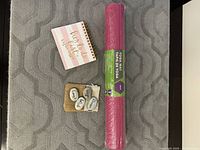 Photo showing the rolled pink Athletic Works yoga mat next to a small spiral-bound notepad labeled 'Her To Do List' and a small drawstring fabric bag containing four engraved stones.