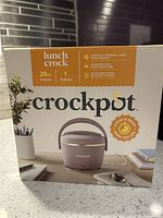 Photo of boxed Crockpot lunch-sized food warmer in blush pink on kitchen counter, showing front packaging image.