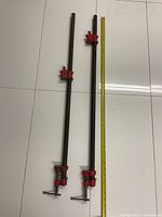 Pair of two vintage heavy duty iron pipe clamps each approximately 36 inches in length, placed on the floor next to a measuring tape showing length.