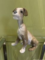 Full side view of the white and brown porcelain terrier figurine sitting upright on a glass surface.