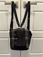Front view of black Tommy Hilfiger knapsack purse hanging from door handles, showing front buckle details and straps