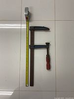 Top view showing the full length of the vintage heavy duty F clamp alongside a tape measure indicating 20 inches length. The metal body has blue paint with some wear; wooden handle is attached to the screw mechanism.