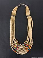 Full view of vintage bib necklace showing multi-strand natural wood beads and colorful square beads in bib section against black background.