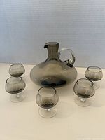 Full view of the smoked glass carafe and five matching glasses arranged around it for display.