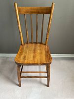 Front view of vintage wooden farmhouse chair showing the plank seat, spindle back, and natural wood finish.