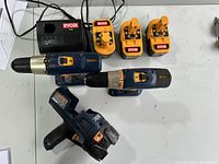 Photo showing Ryobi charger, three 18V batteries, two drill drivers, all on table.