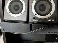 Pair of M-Audio StudioPro 3 studio monitor speakers showing the speaker drivers, front volume knob, headphone and Aux in jacks.