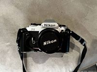 Front view of Nikon FG camera with Nikon body cap and attached strap.