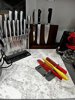 Overview photo showing the DEIK knife block with 6 knives, 3 small colored knives on a gray holder, wooden magnetic knife holder with 3 knives, and a coffee maker on the side