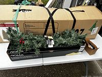Photo showing the 7 ft pre-lit willow Christmas tree packed inside its original cardboard box with black straps securing it.