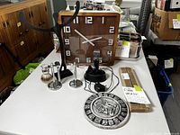Overview of all items in the lot arranged on table including clock, calendar stone, electric razor, shaving kit, iron hand statue, and rebar stakes.