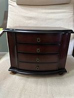 Front view of wooden jewelry box showing four drawers with antique brass pulls and curved front.