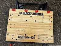 Top view of Black & Decker WorkMate 425 workbench with wooden surface showing measurement scales, brand name, model number, and red clamps.