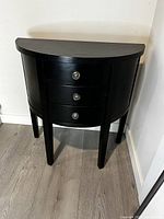 Full front view of black half moon entry table with three drawers and tapered legs.