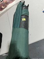 Rolled-up green tent with carrying strap showing a small yellow lot sticker.