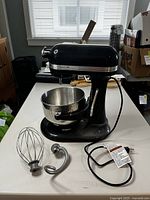 Front perspective of black KitchenAid Professional HD mixer with bowl, wire whisk, dough hook and power cord