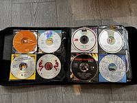 Open black zippered CD case showing two pages of CDs with artists like Ray Charles Super Hits, Big Audio Dynamite, Blade Runner soundtrack and others, each in clear plastic sleeves.