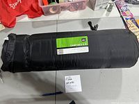 Full view of the black REI Camp Bed 2.5 self-inflating sleeping pad inside its storage bag on a table