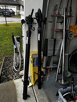 Two black Thule bicycle racks shown upright leaning against a wall with one partially blocking the SportRack kayak carrier box.