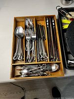 Wooden tray with Gourmet Settings Twist flatware including spoons, forks, knives, and chopsticks neatly organized.