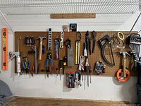 Wide view of pegboard with various hanging hand tools including levels, clamps, saws, pliers, hammers, caulking gun.