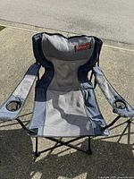 Front view of the Coleman folding chair showing fabric seat and mesh back with Coleman logo and armrests with cup holders.