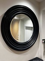 Large round wall mirror mounted on a wall with a thick dark blue frame with concentric rings.