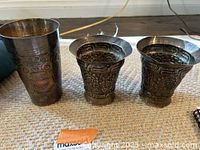 Three silver cups (one tall tumbler and two smaller goblets) arranged on a surface.