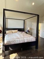 Full view of black wooden canopy California King bed frame, showing posts and headboard with bedding (not included).