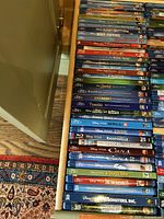 Blu-Ray discs stacked in drawer showing spines with titles mostly Disney and Pixar animated movies including classics and anniversary editions.