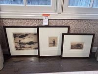 Three sepia-tone etchings in brown wooden frames leaning against wall