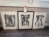 Three Gian Antonio abstract figure drawings from 1970 positioned against a wall. Center one is framed; the left and right ones are unframed and in plastic.