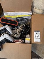 View into box showing two PS5 controllers, portable speaker, cables, remotes, and user manual packets