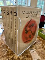Volumes 1-5 Modernist Cuisine in clear acrylic slipcase upright on counter