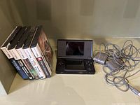 Front view of open black DS Lite with power adapter and five game cases