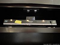 Wide front view of the Panasonic Blu-Ray player with a note attached, showing overall appearance and branding.