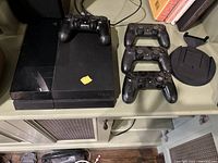 Overview showing PS4 console on shelf with four controllers and circular stand
