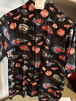Front view of black Reyn Spooner Pixar Cars Aloha shirt showing all-over prints of Lightning McQueen, Mack truck, Rust-eze logos and fireworks.