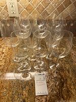 Twelve Riedel wine glasses arranged on countertop with label indicating Riedel glasses for sale.