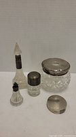 Five antique cut glass containers with silver or silver-toned tops arranged together showing size and detail.